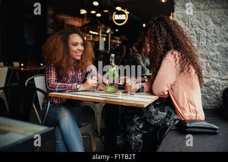 Two young women talking sitting in a restaurant. African woman smiling and chatting with her friend in a cafe. Stock Photo
