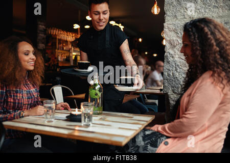 Waiter serving coffee to young women at restaurant. Two female friends at coffee shop. Stock Photo