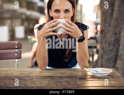Young woman drinking coffee at a cafe and looking at the camera. Caucasian female sitting at table having a cup of coffee at caf