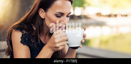 Close up portrait of young woman with an aromatic coffee in hands. Female drinking coffee at cafe.