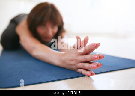 Woman doing stretching workout on fitness mat with her hands clasped. Fit female doing yoga on exercise mat at gym. Focus on han Stock Photo