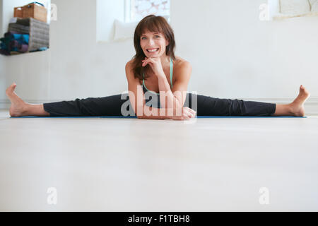 Happy woman doing wide angle seated forward bend yoga at gym. Fitness female practicing Upavistha Konasana yoga. Caucasian woman Stock Photo