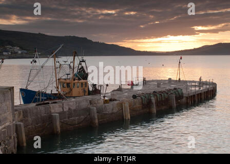 Fishing boat moored next to a pier at TThe Cobb Harbour in Lyme Regis on Dorset's Jurassic Coast., England, UK Stock Photo