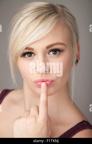 Pretty teenage girl with a finger pressed against her lips. Stock Photo