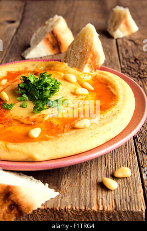 Hummus with parsley, pine nuts on plate and rustic wooden background close up Stock Photo