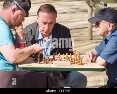 Garden Chess Game: making a move. Two Parisians play chess in the Jardin du Luxembourg one watches intently as a player moves. Stock Photo