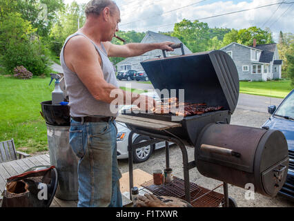 A man smokes a cigar and barbecues chicken on a charcoal grill. Stock Photo