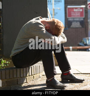Man sat on low wall with his head buried in his hands in Bedford, Bedfordshire, England Stock Photo