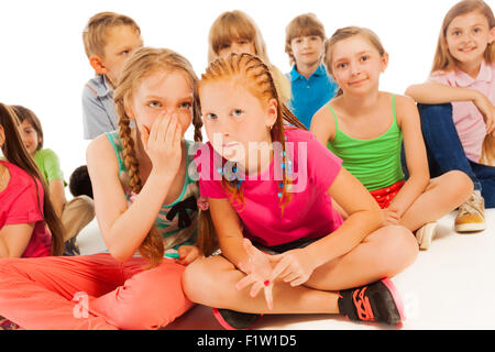 Two whispering girls sit among other friends Stock Photo