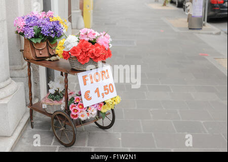 A cart with over wicker baskets and an old wicker fishing basket full of flowers for sale Stock Photo