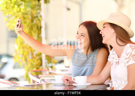 Happy tourist friends taking a selfie photo with smartphone in a coffee shop terrace Stock Photo