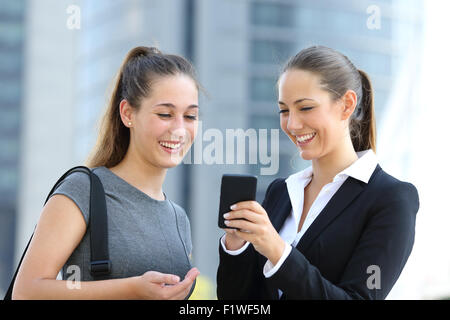 Two businesswomen talking about smart phone in the street with office buildings in the background