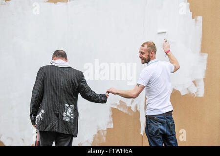 A man using a roller to paint a wooden wall. Stock Photo