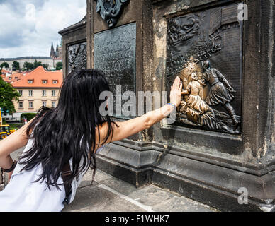 Female tourist touching a  bronze plaque for luck on the St John of Nepomuk statue, Charles bridge,Prague,Czech Republic. Stock Photo