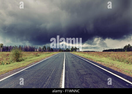 asphalt road and dark thunder clouds over it . Stock Photo