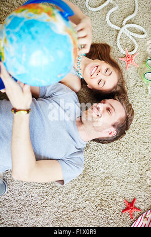 Smiling couple of adventurers pointing at globe while lying on the floor Stock Photo