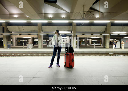 Passenger with red rolling trolley suitcase waiting for a train on a railway station platform Stock Photo