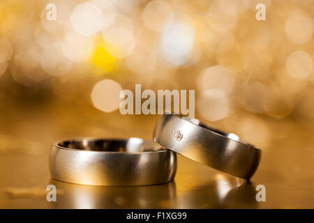 Silver or platinum wedding rings on golden surface, sparkling bokeh in background Stock Photo
