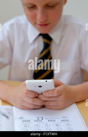 School pupil distracted by using a mobile phone (texting) whilst sat at his desk with his course work home work Stock Photo