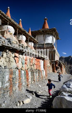 Nepal, Gandaki zone, Upper Mustang (near the border with Tibet), boys running along a mani wall (stones inscribed with a buddhist mantra) and stupa (chorten) in the village of Tangge Stock Photo