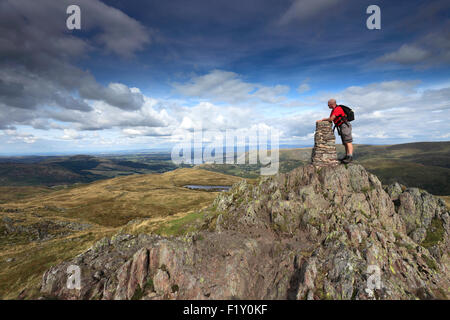 Walker at the Summit cairn and OS Trig Point on Place Fell, Lake District National Park, Cumbria, England, UK. Stock Photo