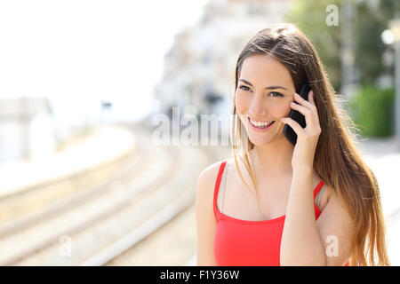 Lady talking on the mobile phone while is waiting in a train station in summer Stock Photo