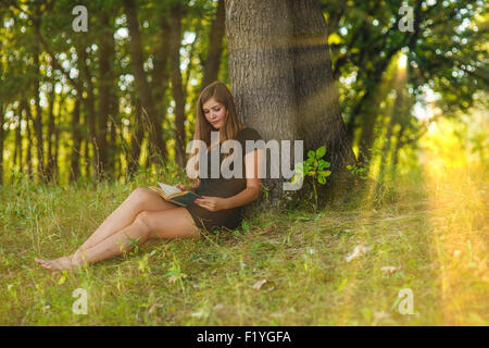 woman girl sits reading a book under a tree in the forest park o Stock Photo