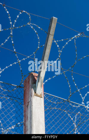 Prison concrete pillar and barbed wire fence against blue sky, security concept Stock Photo