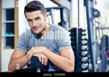 Portrait of a happy man sitting on the bench with dumbbells at gym Stock Photo