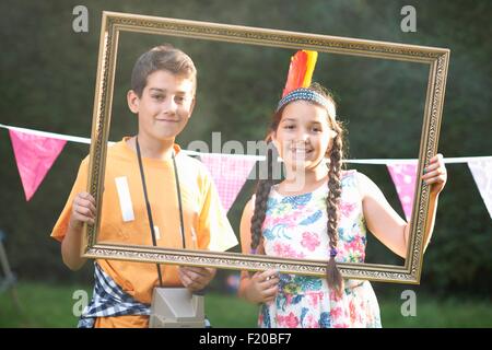 Boy and girl looking through picture frame, smiling, looking at camera Stock Photo