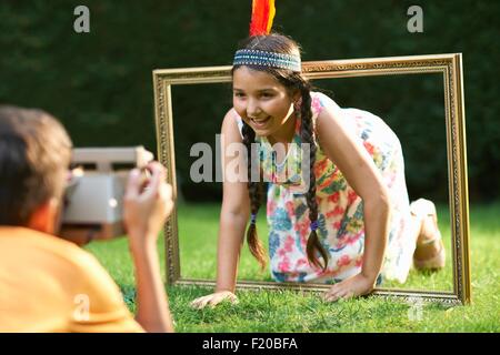 Girl kneeling, looking through picture frame, having photograph taken Stock Photo