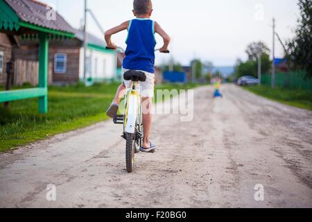 Young boy, riding bicycle along dirt road, rear view Stock Photo