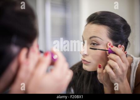Over the shoulder mirror image of young woman applying mascara Stock Photo