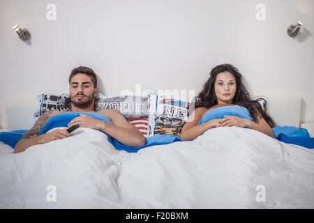 Young couple lying in bed sulking Stock Photo