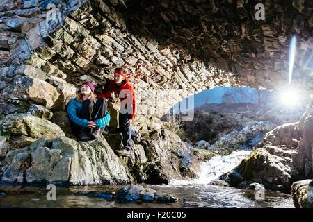 Young couple hiking, resting under bridge, Ashness Bridge, Keswick, Lake District, Cumbria, United Kingdom Stock Photo