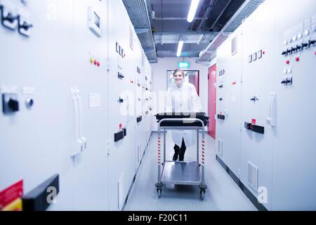 Portrait of young female scientist pushing trolley in technical room Stock Photo