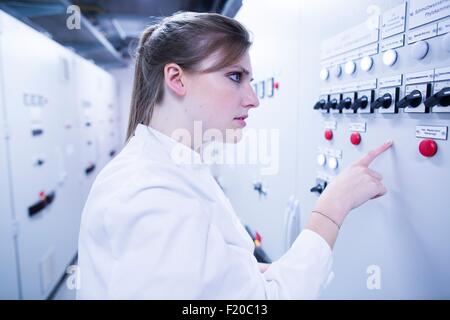 Young female scientist pointing at machine in technical room Stock Photo
