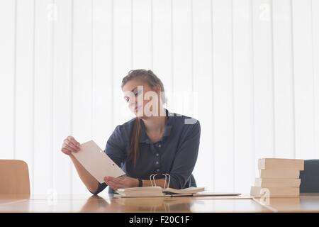 Young female student reading file index card at library desk Stock Photo