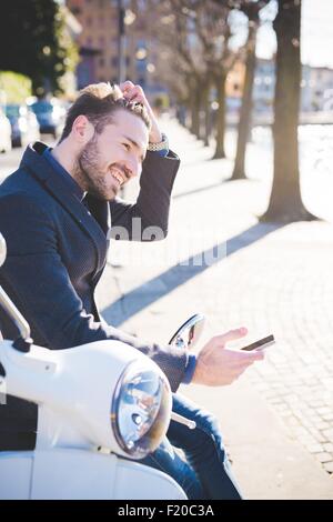 Stylish young man sitting on moped with smartphone Stock Photo