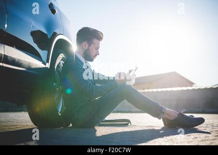 Stylish young man sitting leaning against car using digital tablet Stock Photo