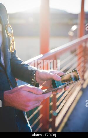 Cropped close up of young mans hands using digital tablet and smartphone on footbridge Stock Photo