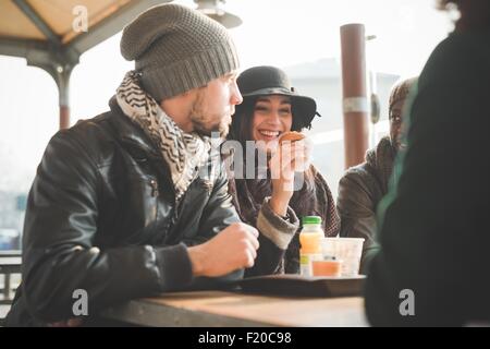 Four young adult friends chatting and eating doughnuts at sidewalk cafe Stock Photo