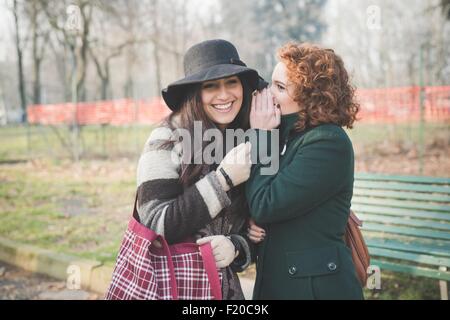 Two female adult friends whispering in park Stock Photo