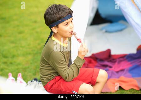 Boy eating ice lolly in front of homemade tent in garden Stock Photo