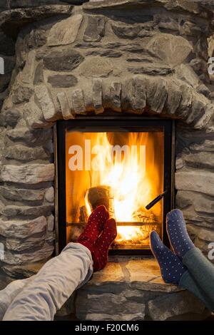 Cropped shot of two young women with feet up in front of fireplace Stock Photo