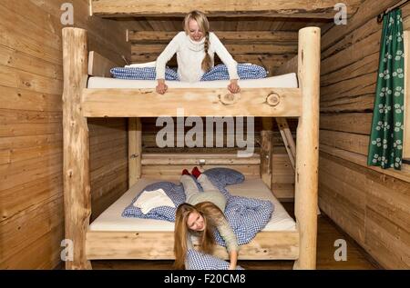 Two young women friends fooling around on bunk beds in log cabin Stock Photo