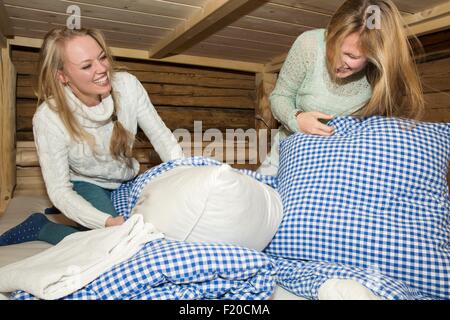 Two young women friends having pillows fight in log cabin Stock Photo