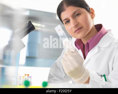 Female scientist in lab testing blood sample using microscope Stock Photo