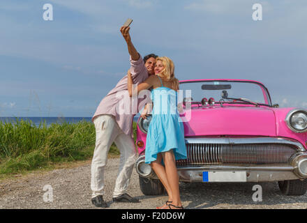 Young couple posing for selfie with vintage convertible, Havana, Cuba Stock Photo