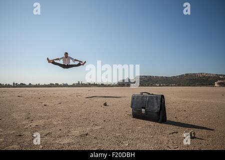 Mid adult businessman jumping mid air at beach Stock Photo